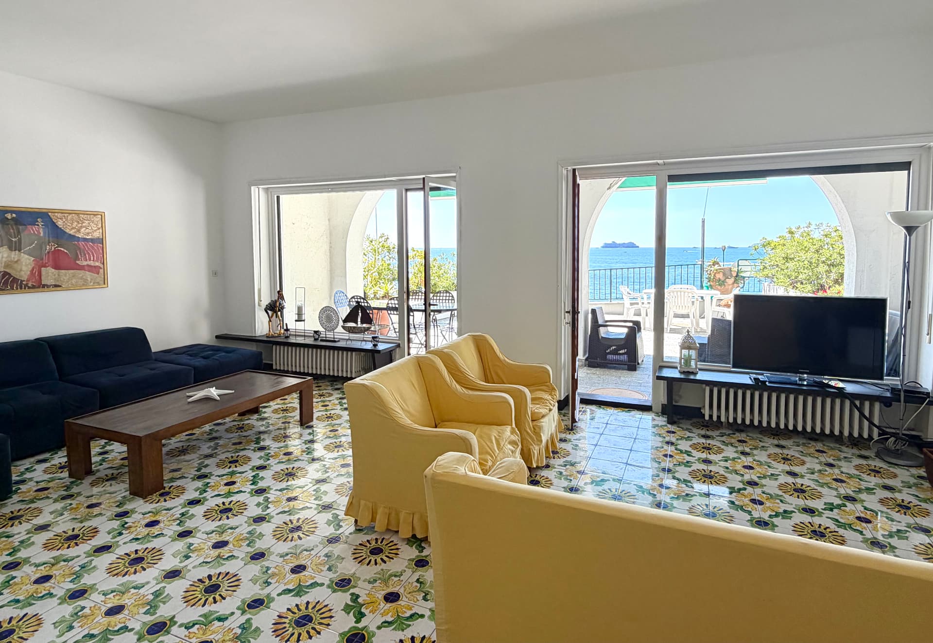 Salon with navy sectional, yellow armchairs and open sea-view doors